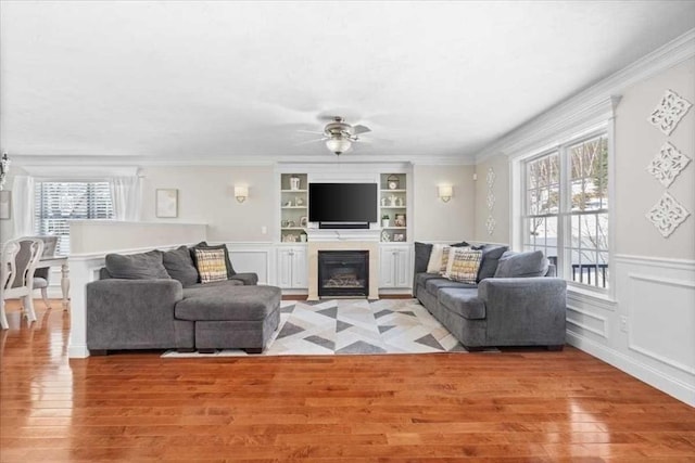 living area featuring crown molding, a decorative wall, a ceiling fan, and light wood-style floors