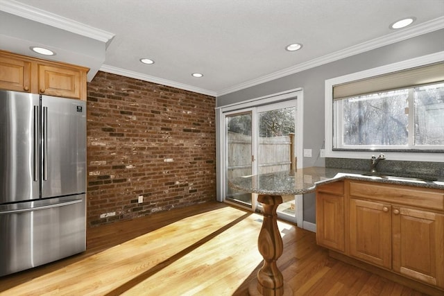 kitchen featuring wood finished floors, brick wall, freestanding refrigerator, ornamental molding, and a sink