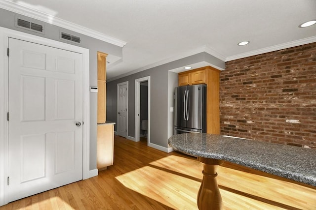 kitchen with brick wall, visible vents, freestanding refrigerator, and light wood-type flooring