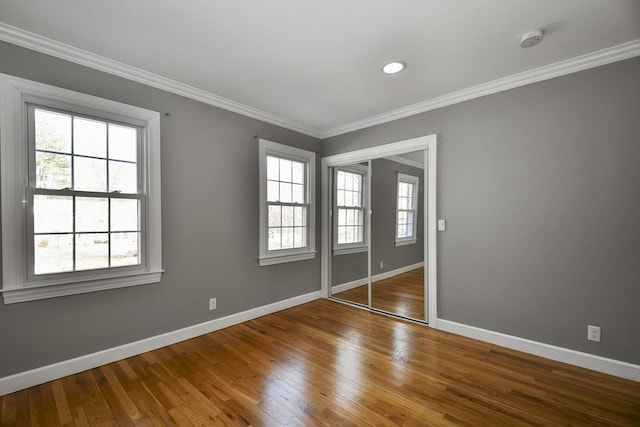 unfurnished bedroom featuring a closet, crown molding, baseboards, and hardwood / wood-style floors