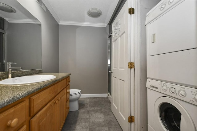 bathroom with vanity, stacked washer / drying machine, crown molding, toilet, and tile patterned floors