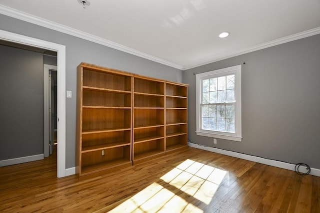 empty room featuring wood finished floors, baseboards, and ornamental molding