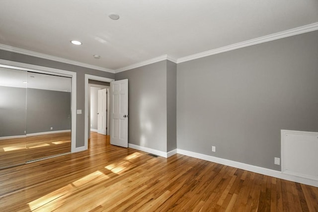 unfurnished bedroom featuring crown molding, wood finished floors, baseboards, and a closet