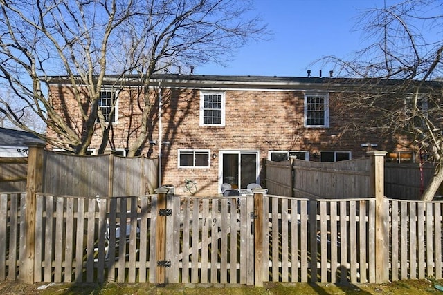 back of house with brick siding, fence private yard, and a gate