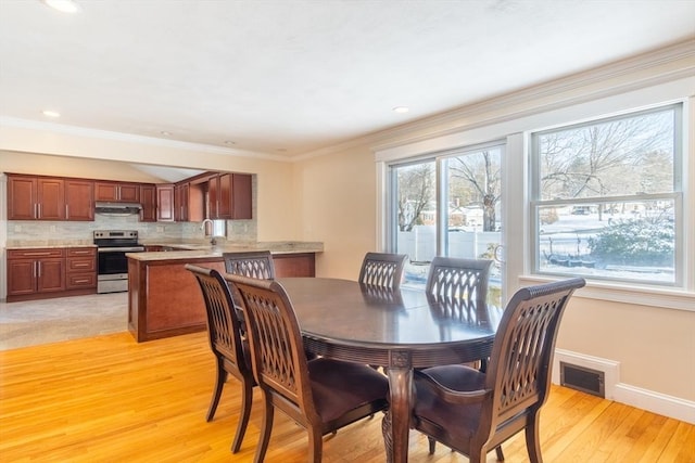 dining room with crown molding, a healthy amount of sunlight, and light hardwood / wood-style flooring