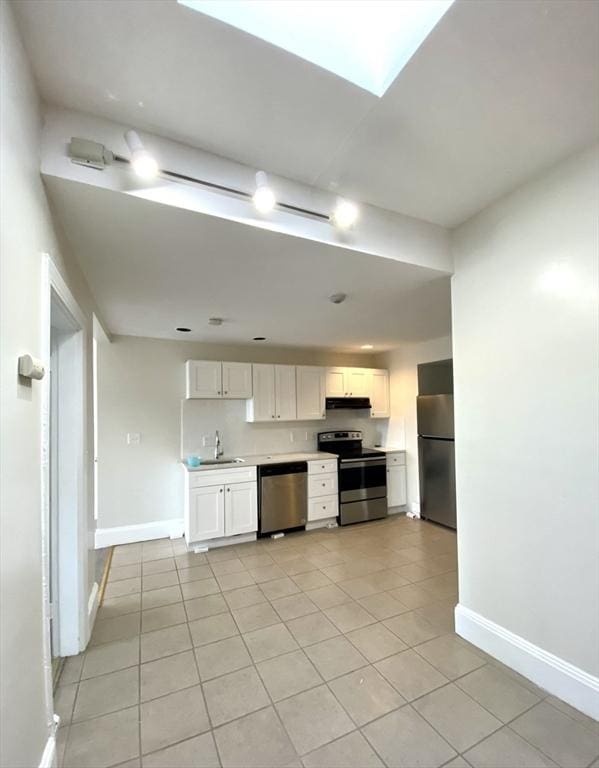 kitchen featuring sink, a skylight, light tile patterned floors, appliances with stainless steel finishes, and white cabinets