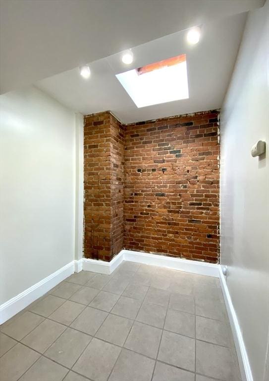 additional living space with light tile patterned flooring, brick wall, and a skylight