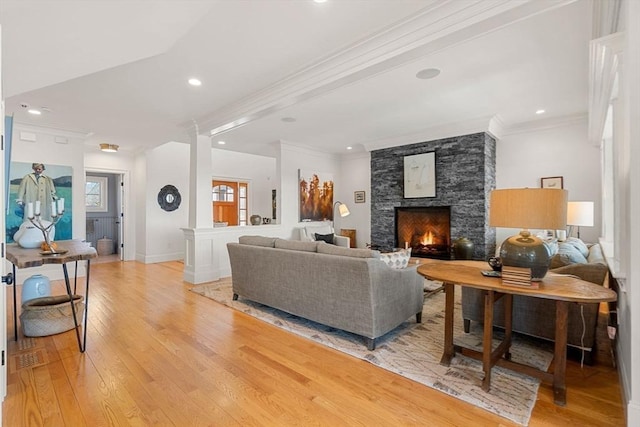 living room featuring light wood-style floors, crown molding, recessed lighting, and a stone fireplace