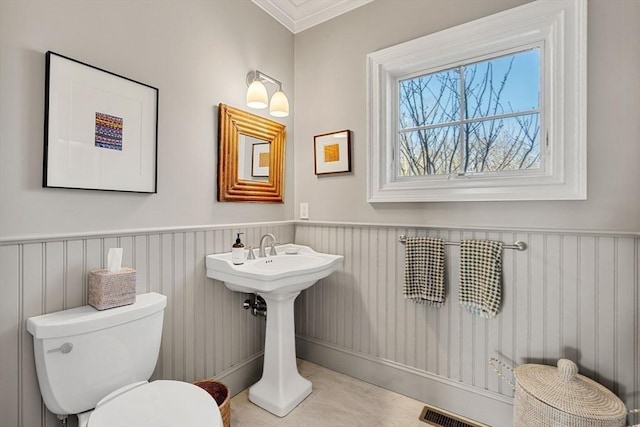 half bathroom featuring visible vents, ornamental molding, a wainscoted wall, and toilet