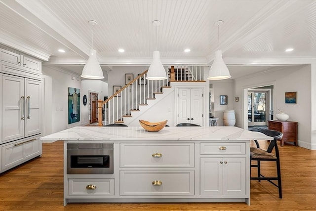 kitchen featuring crown molding, pendant lighting, a kitchen island with sink, light wood-style floors, and light stone counters
