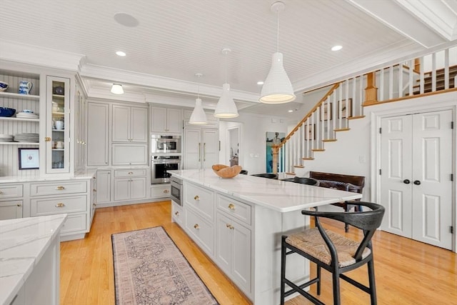 kitchen featuring a breakfast bar area, light wood-style flooring, a center island, ornamental molding, and glass insert cabinets