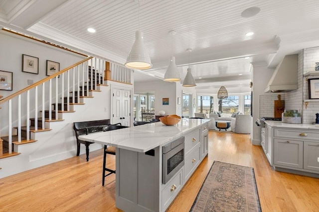 kitchen with open floor plan, premium range hood, plenty of natural light, stainless steel microwave, and gray cabinetry