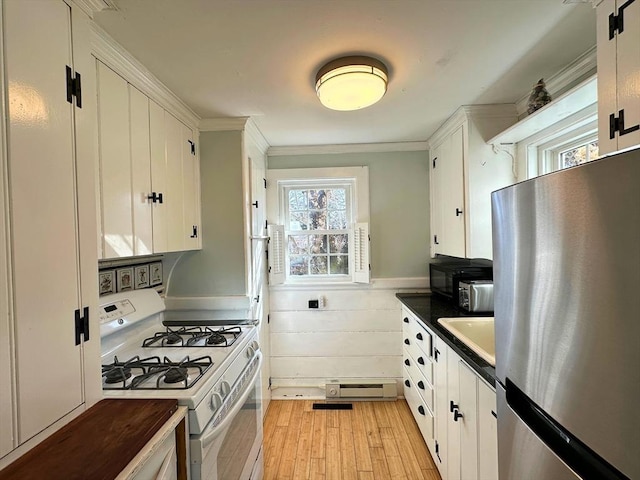 kitchen with light wood finished floors, white gas stove, freestanding refrigerator, white cabinets, and dark countertops