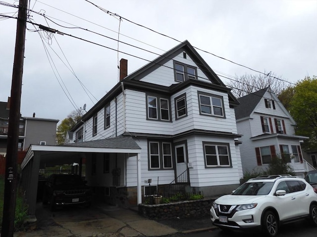 view of front of house featuring entry steps, a chimney, an attached carport, and a shingled roof