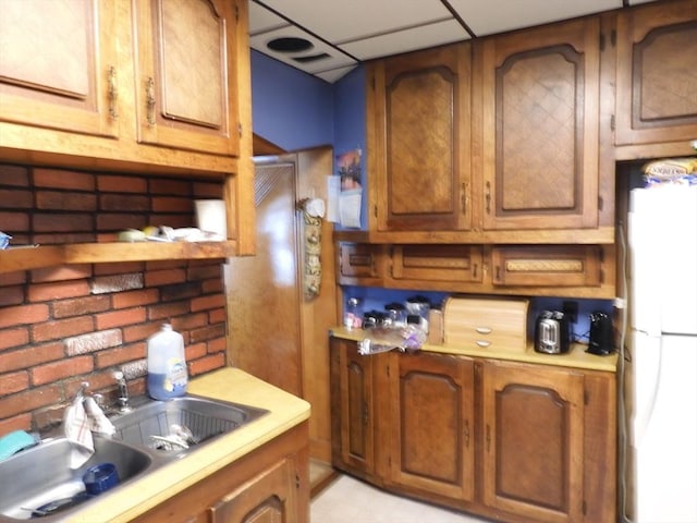 kitchen with light countertops, freestanding refrigerator, brown cabinets, and a sink