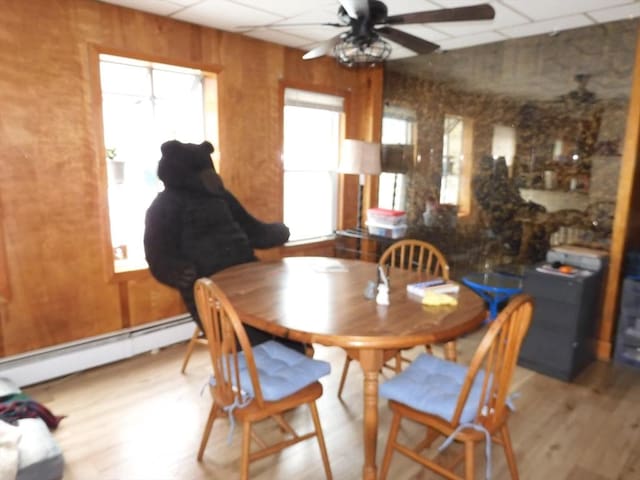 dining area featuring baseboard heating, a ceiling fan, a paneled ceiling, and wood finished floors