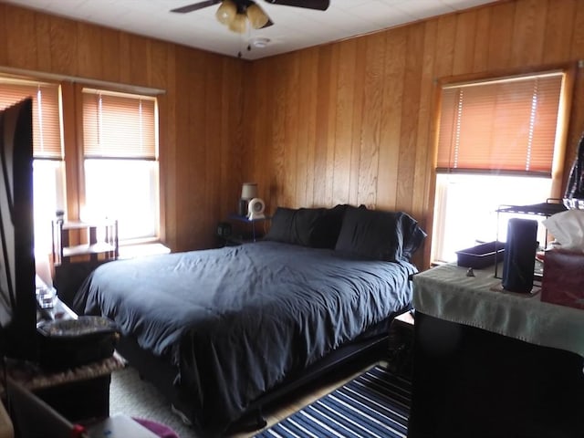 bedroom with wood walls, a ceiling fan, and multiple windows