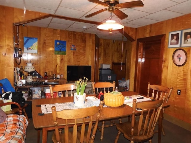 dining space featuring a paneled ceiling, ceiling fan, and wooden walls