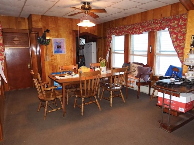 dining area featuring carpet floors, ceiling fan, and wood walls