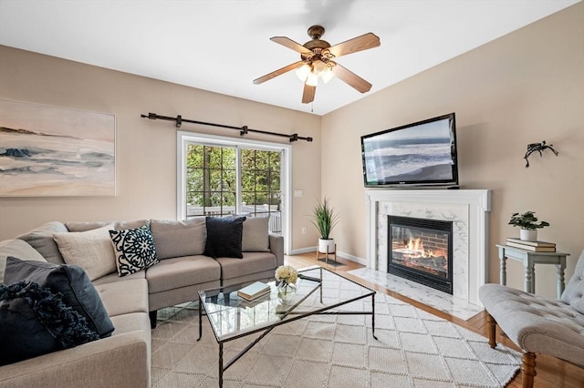 living area featuring a ceiling fan, a fireplace, light wood finished floors, and baseboards
