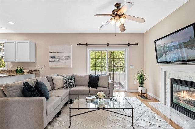 living room with light wood-style floors, recessed lighting, baseboards, a ceiling fan, and a high end fireplace