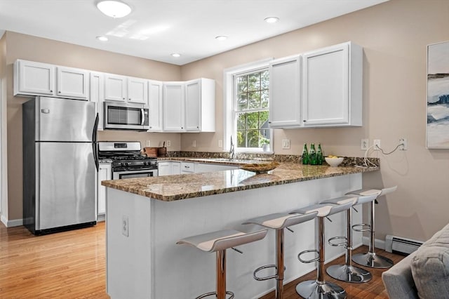 kitchen with stainless steel appliances, dark stone countertops, a peninsula, white cabinets, and recessed lighting