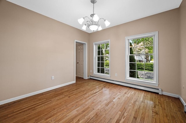 spare room featuring baseboard heating, a chandelier, baseboards, and light wood-type flooring