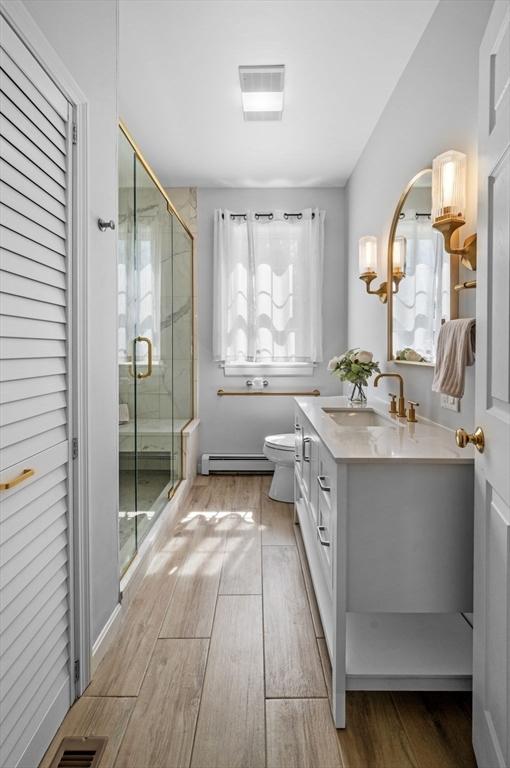 bathroom with a baseboard heating unit, wood finished floors, plenty of natural light, and a stall shower