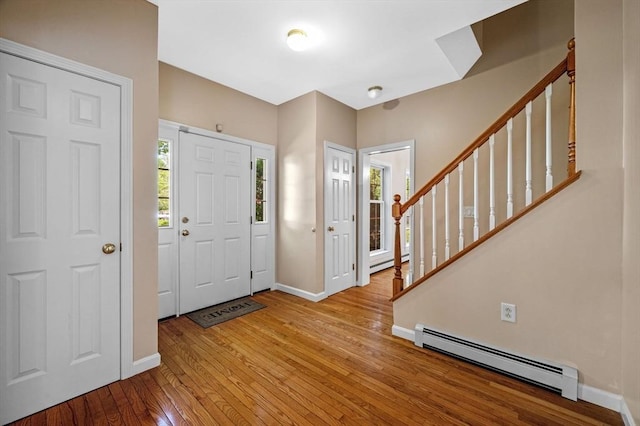 foyer featuring a baseboard heating unit, hardwood / wood-style floors, baseboards, and stairs