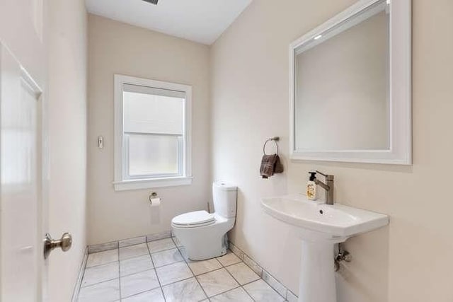 half bath with toilet, baseboards, and tile patterned flooring