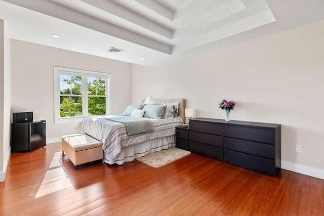 bedroom featuring wood finished floors, a tray ceiling, and baseboards