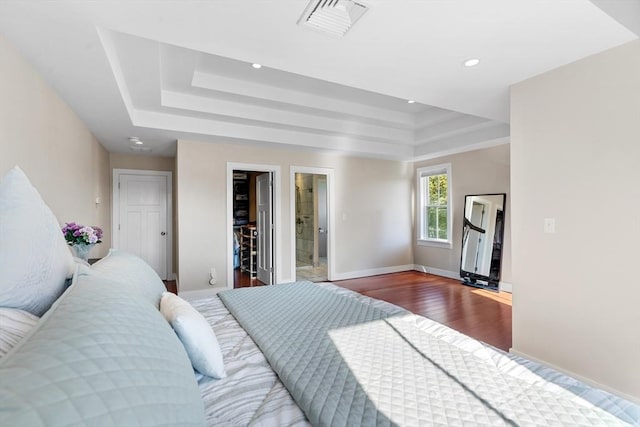 bedroom featuring a raised ceiling, wood finished floors, recessed lighting, baseboards, and a walk in closet
