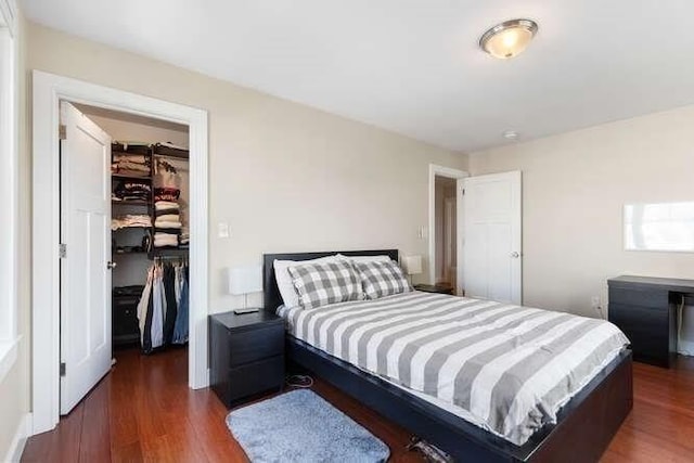bedroom with a walk in closet, dark wood-style flooring, and a closet