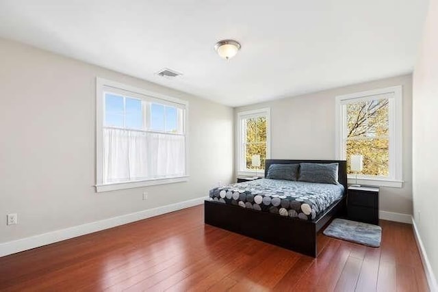 bedroom with multiple windows, wood-type flooring, and baseboards