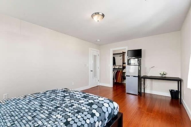 bedroom with wood finished floors, a spacious closet, and baseboards