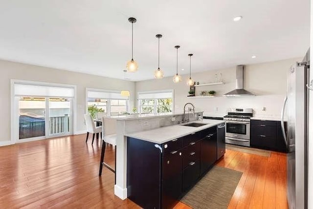 kitchen featuring wall chimney exhaust hood, appliances with stainless steel finishes, a sink, dark cabinets, and a breakfast bar