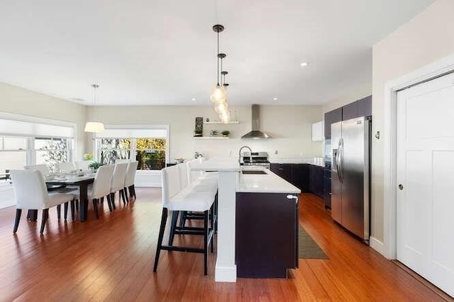 kitchen with stainless steel fridge, wall chimney range hood, light countertops, wood finished floors, and recessed lighting