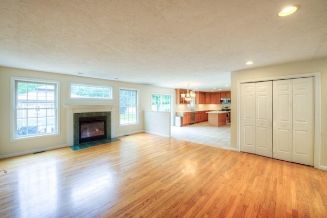 unfurnished living room with a healthy amount of sunlight, a high end fireplace, a textured ceiling, and light wood-type flooring