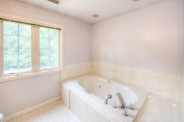 bathroom with a relaxing tiled tub, toilet, and tile patterned flooring