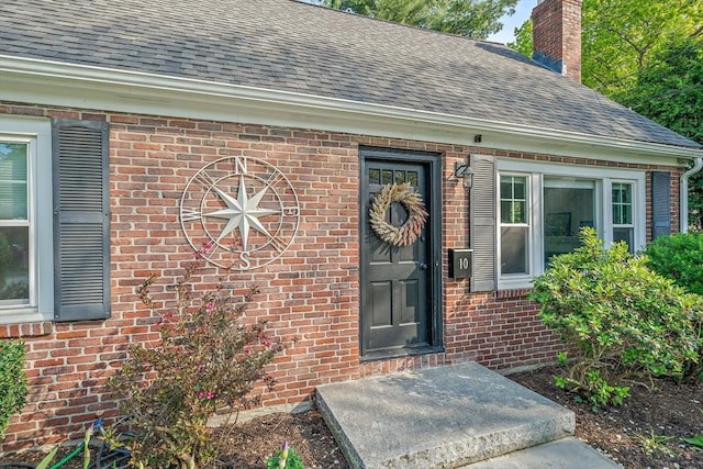 10 Stoughton Rd, Dedham, MA 02026 - view of exterior entry featuring roof with shingles, brick siding, and a chimney