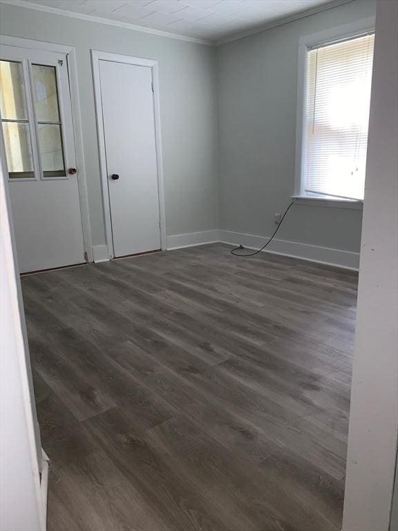 spare room with crown molding, dark wood-type flooring, and baseboards