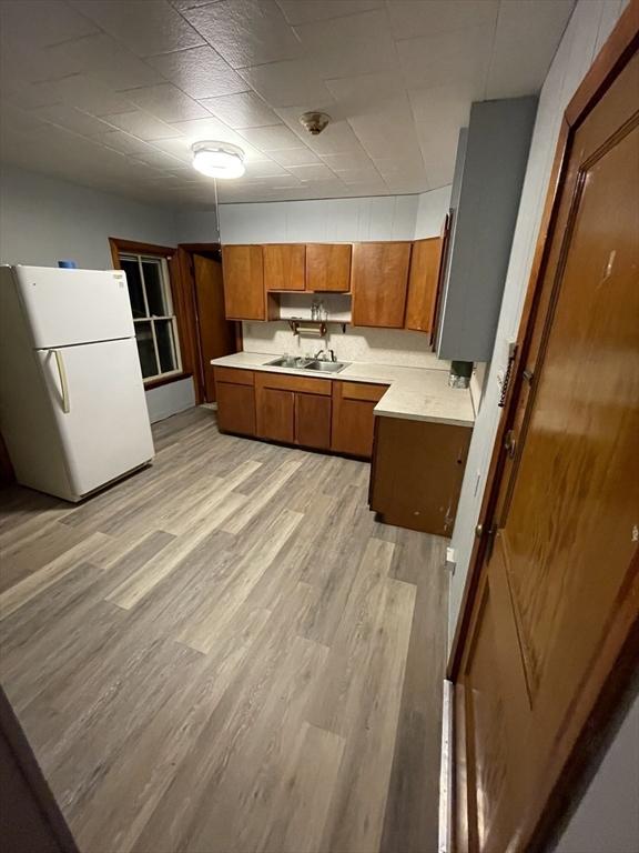 kitchen featuring freestanding refrigerator, brown cabinetry, light countertops, light wood-style flooring, and a sink
