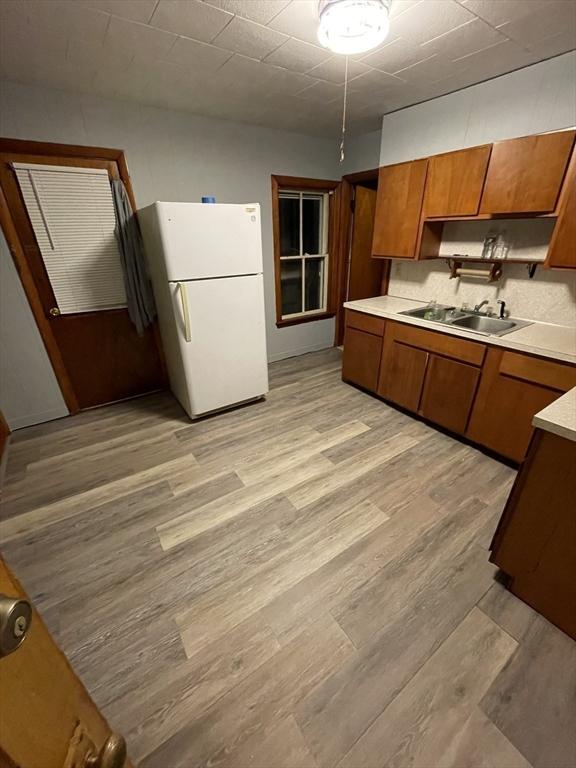 kitchen featuring freestanding refrigerator, a sink, brown cabinetry, light countertops, and light wood-style flooring