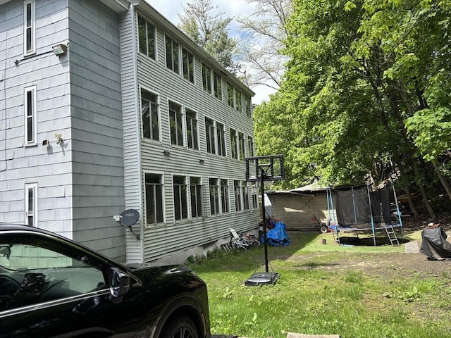 view of side of property with a trampoline and a lawn