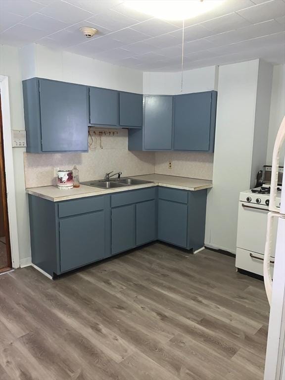 kitchen featuring light countertops, blue cabinets, a sink, dark wood-style flooring, and white range oven
