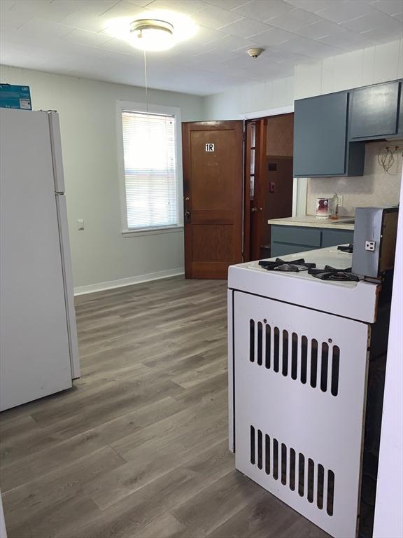 kitchen featuring freestanding refrigerator, gas range oven, wood finished floors, and baseboards