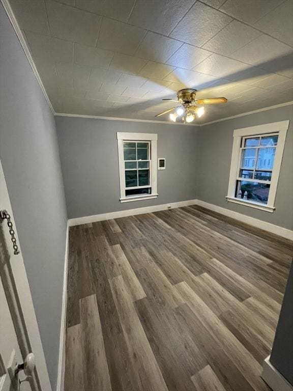empty room with ornamental molding, wood finished floors, a ceiling fan, and baseboards