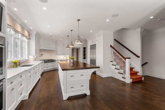 kitchen featuring white cabinets, dark wood-style flooring, a sink, recessed lighting, and a center island with sink