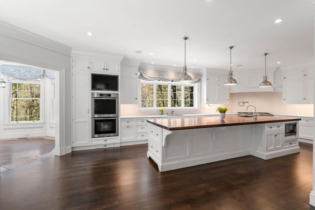 kitchen featuring stainless steel appliances, wooden counters, a healthy amount of sunlight, and white cabinetry
