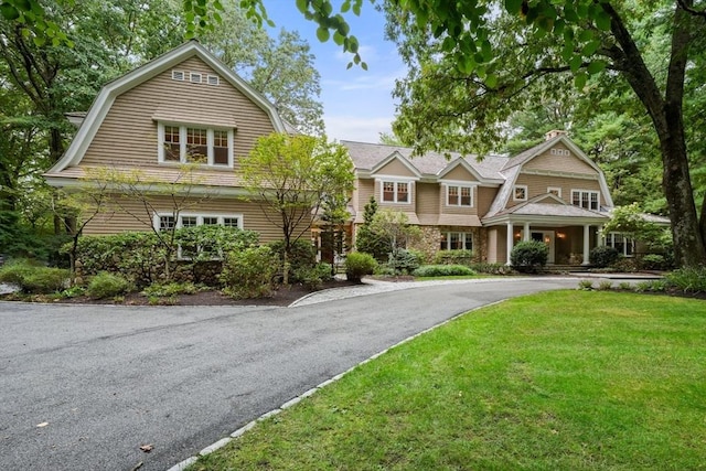 view of front of home featuring aphalt driveway, a porch, a gambrel roof, and a front yard